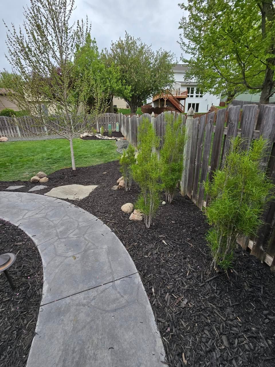 A concrete walkway leading to a wooden fence in a backyard.