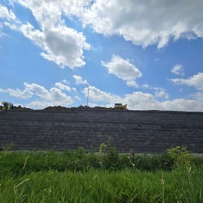 A large brick wall is being built on top of a grassy hill.
