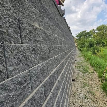 A person is standing on top of a brick wall next to a gravel path.