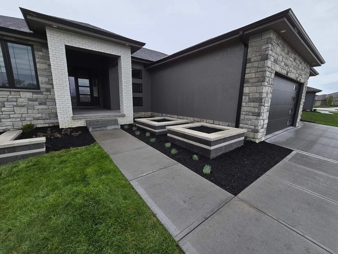 A modern house exterior with dark gray walls, white stone accents, a garage, and two concrete planters by the walkway.