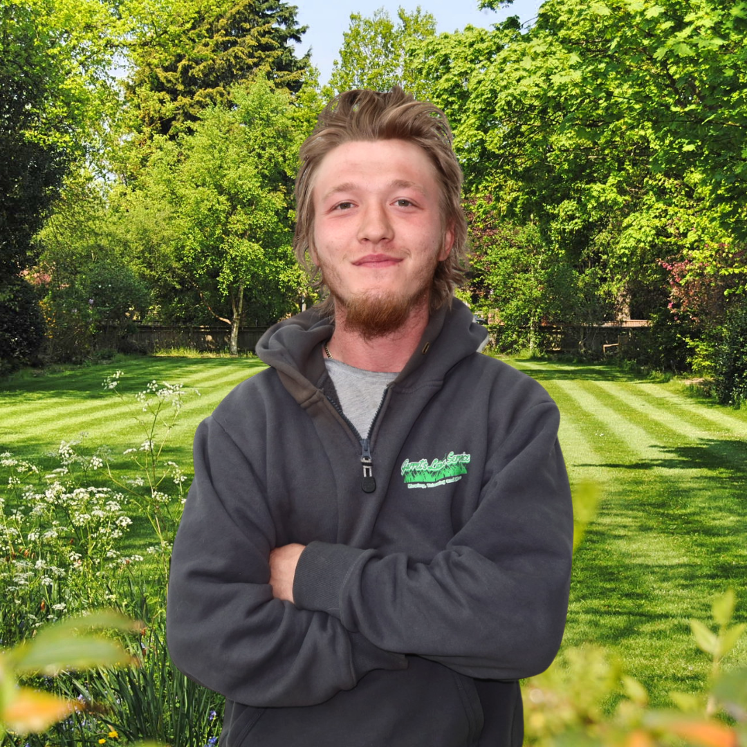 A man is standing in a garden with his arms crossed and smiling.
