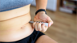 A person holds an injection pen against the skin of their abdomen to self-administer medication.