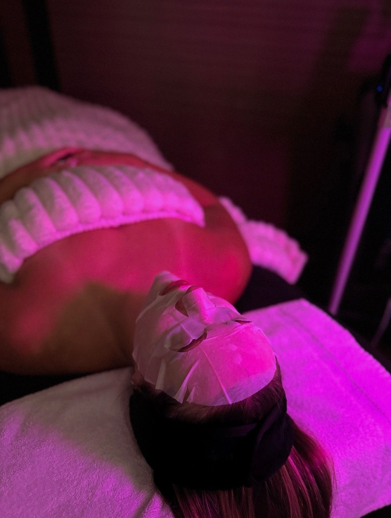 A technician uses a handheld cosmetic device to perform a facial treatment on a person lying down with a headband.