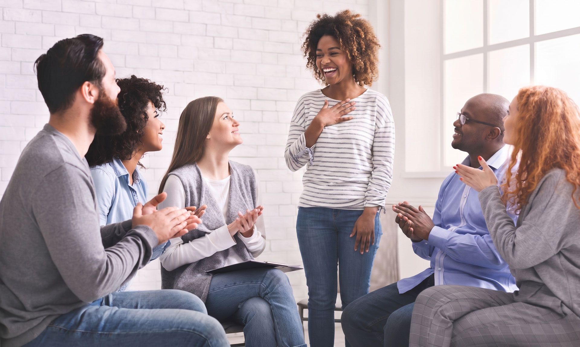 Small group seated in a circle, talking and smiling in a bright room with a whiteboard.