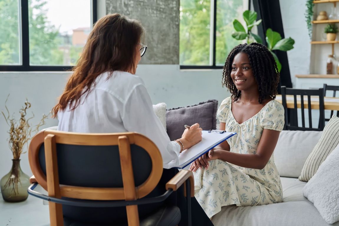 Therapist taking notes while speaking with a smiling client in a bright living room