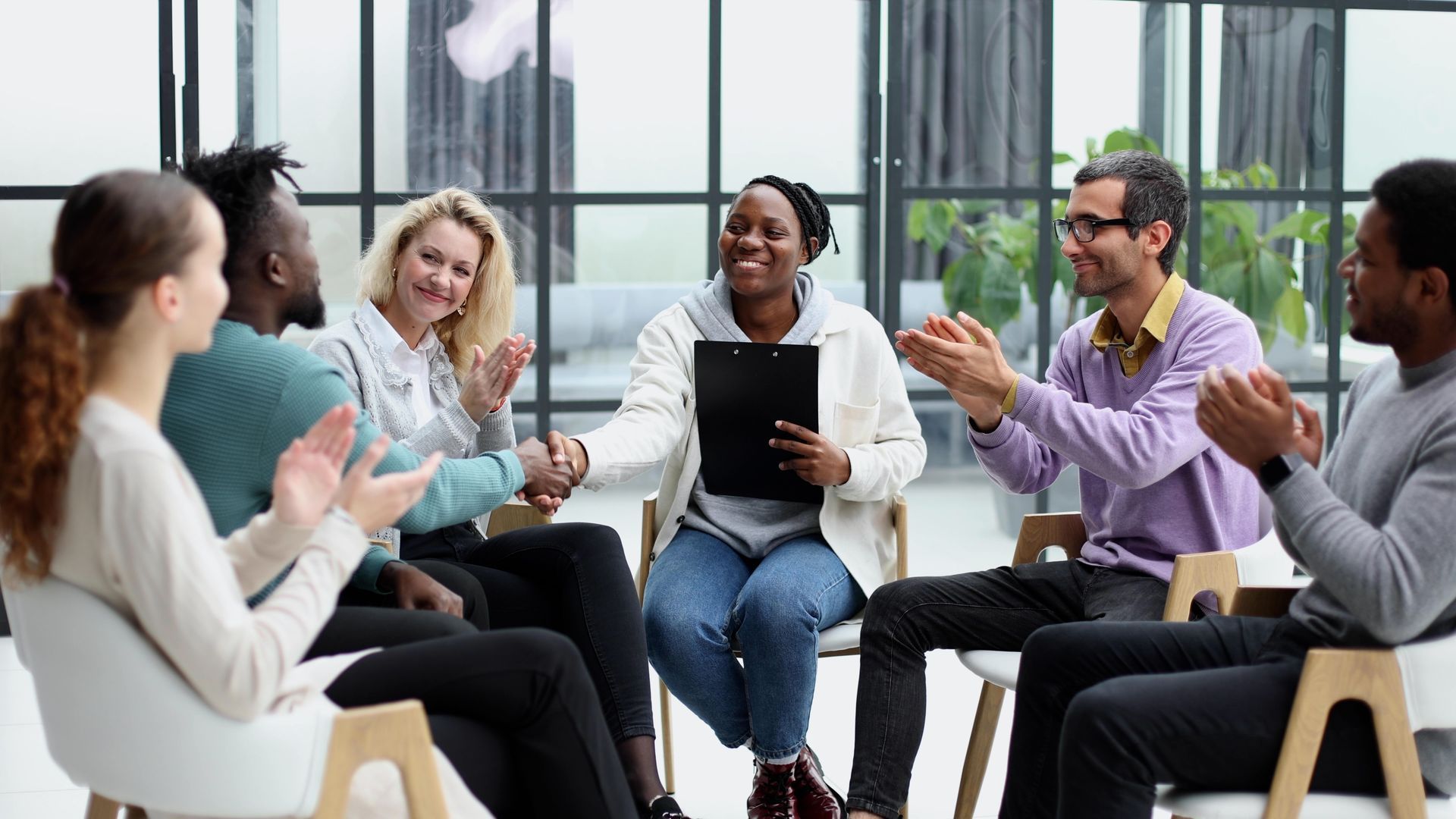 People seated in a bright office meeting, smiling and clapping during a group discussion.