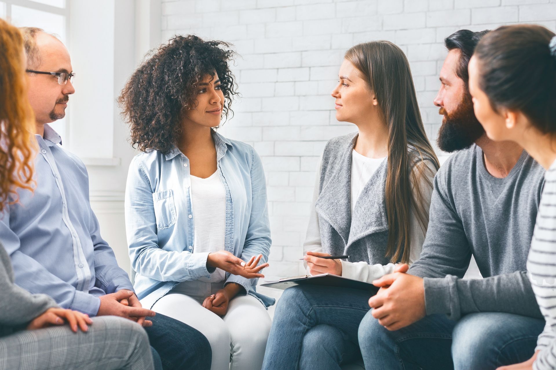People seated in a circle, talking in a bright room during a group discussion.