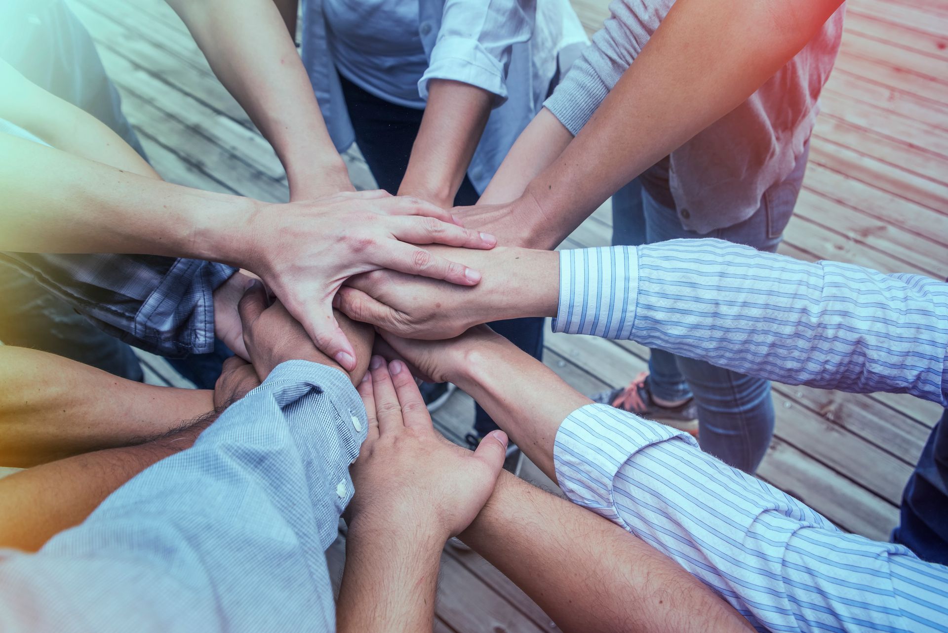 Hands stacked together in a teamwork gesture over a wooden floor