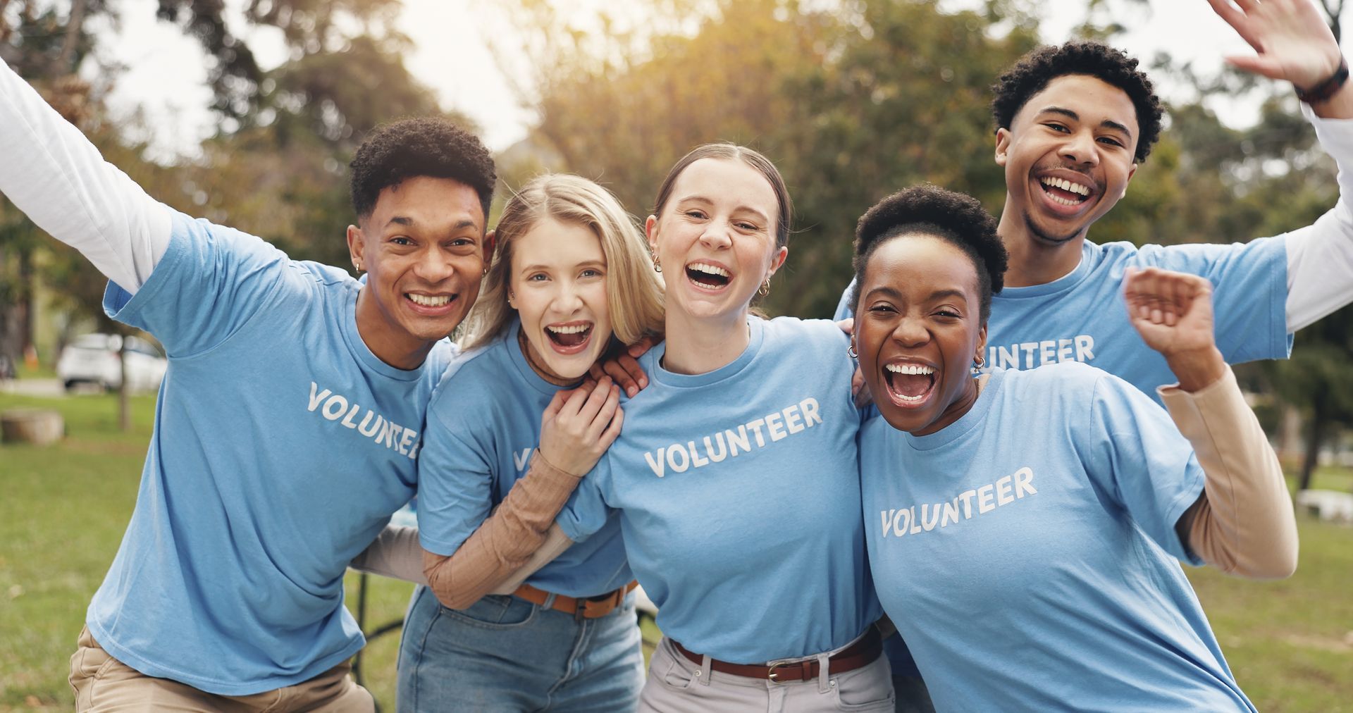 Five smiling volunteers in blue shirts pose outdoors with arms around each other