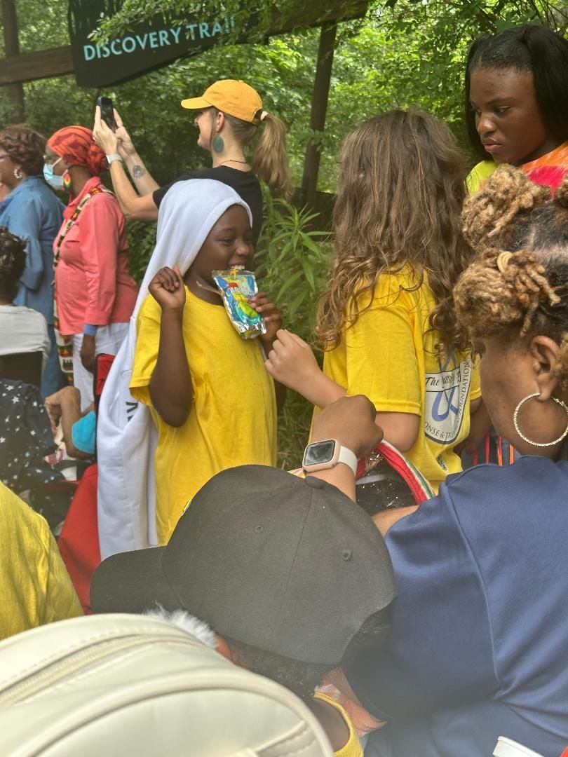 Children gathered outdoors, one in a white hooded garment holding a colorful object.