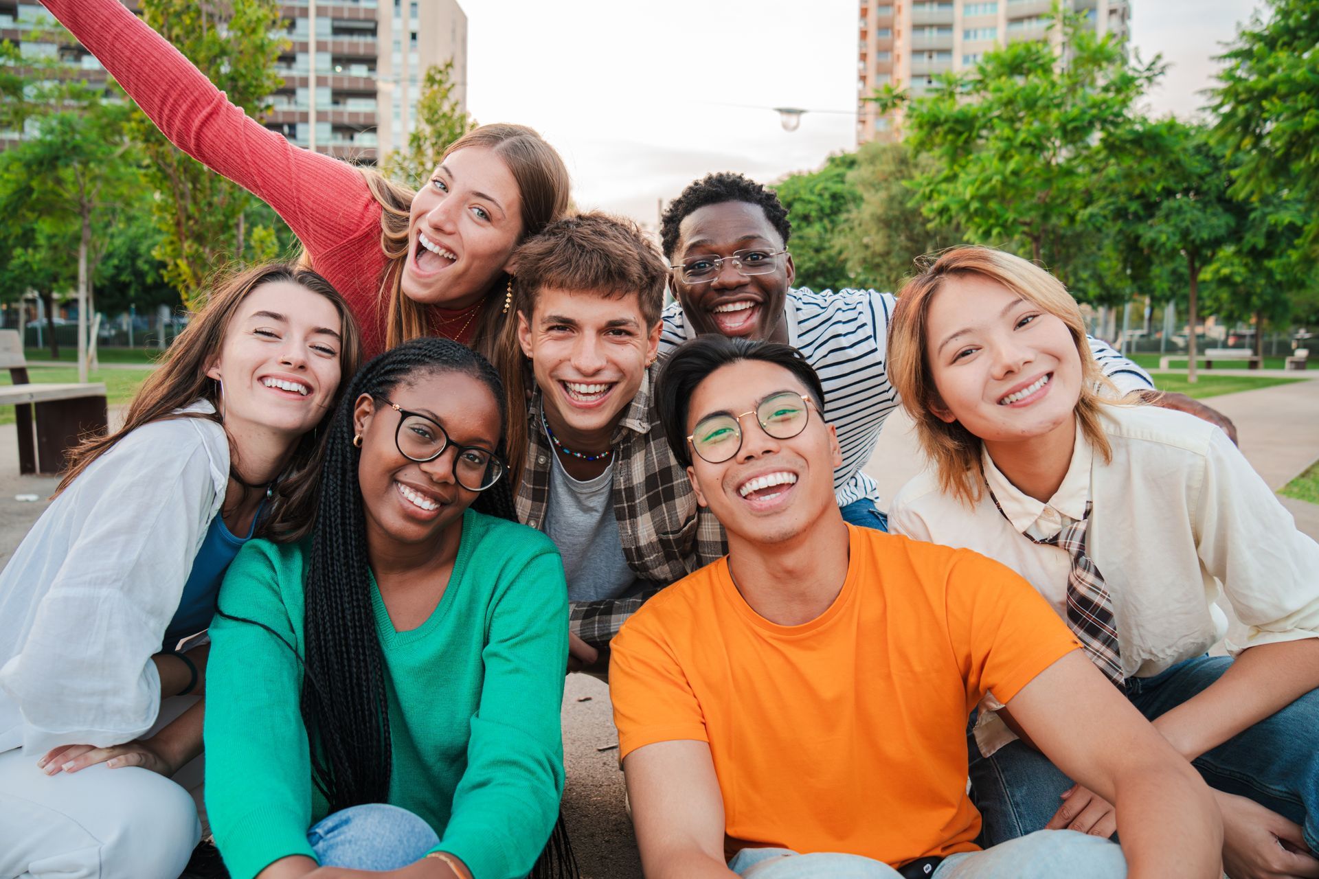 Smiling group of friends posing outdoors in a park, with city buildings and trees behind them