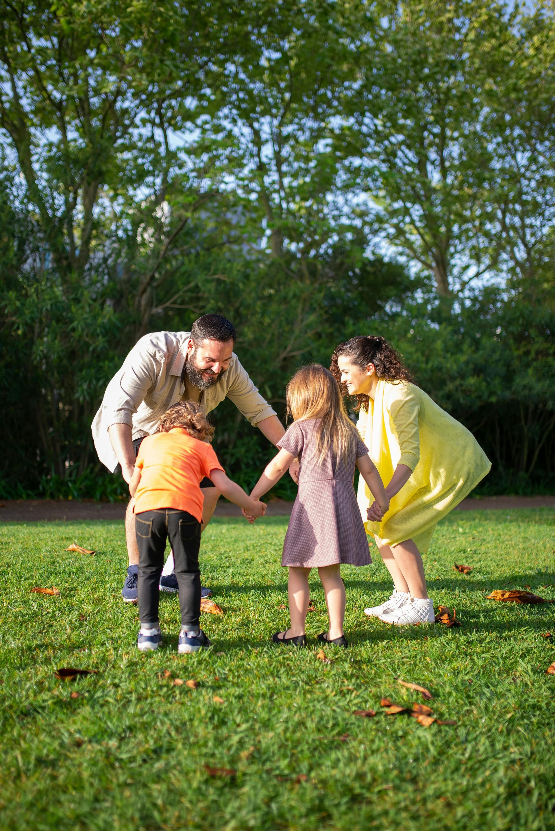 A family in a sunlit park holds hands in a circle on the grass.