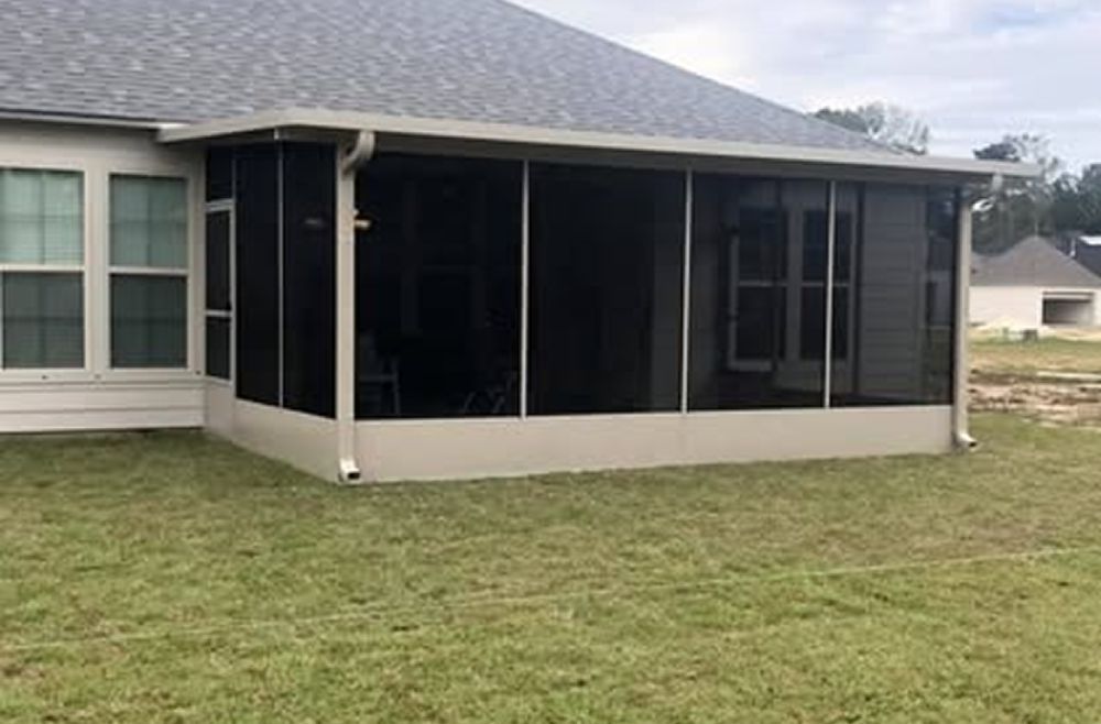 Screened porch attached to a beige house with dark screens, set on a green lawn.
