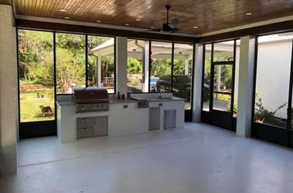 Outdoor kitchen with white countertops, grill, and sink inside a screened enclosure.