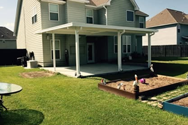A backyard with a two-story house and covered patio. There is a sandbox and lawn furniture.