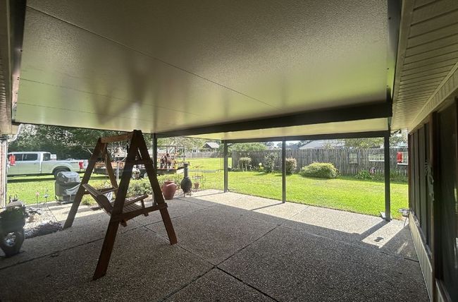 Covered patio with a swing set, screening, and view of a yard.