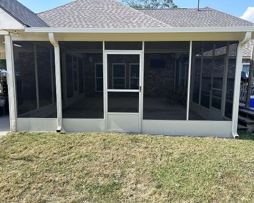 Screened-in porch attached to a house with beige frames, dark screens, and a door, on a grass lawn.