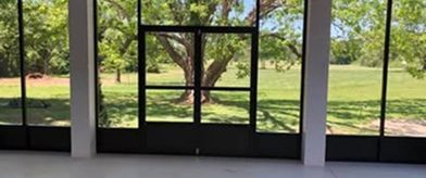 Interior view of a building with large glass doors and windows overlooking a grassy field with trees.