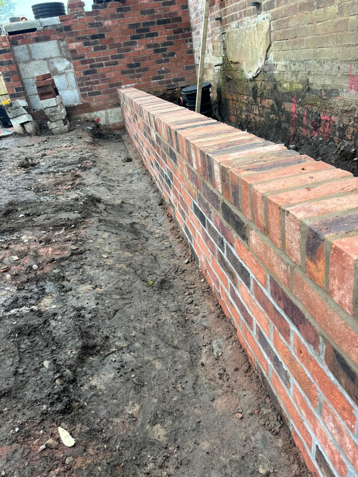 Partially built brick wall beside a muddy construction site and unfinished brick buildings