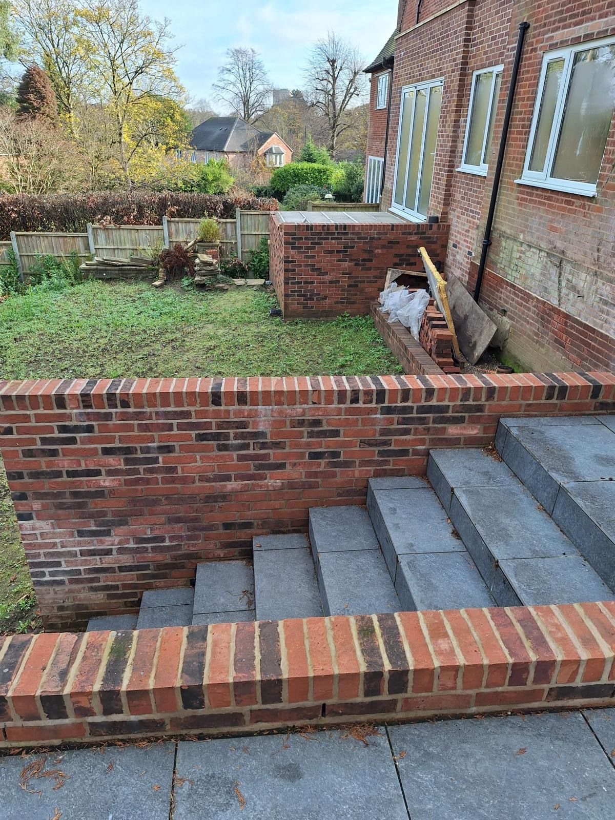 Brick steps beside a red-brick house lead down to a small garden with a low wall and grass.
