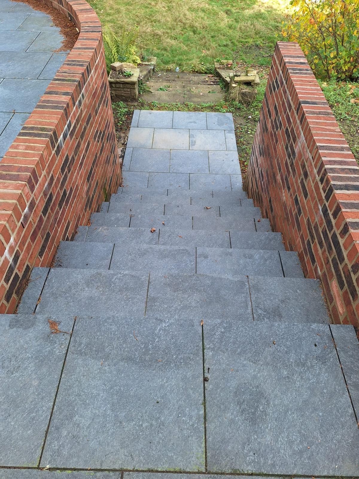 Stone steps between brick walls leading down to a grassy path outdoors