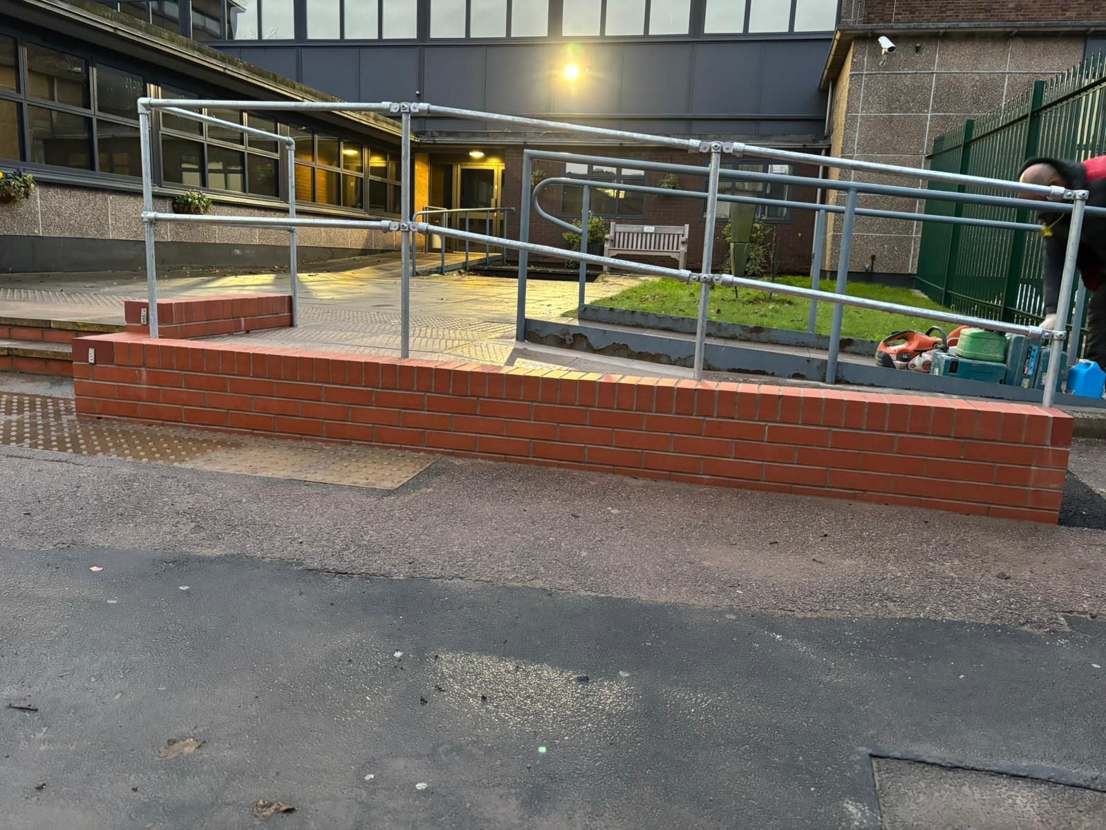Bricked ramp with metal railings leading to a building entrance in a courtyard