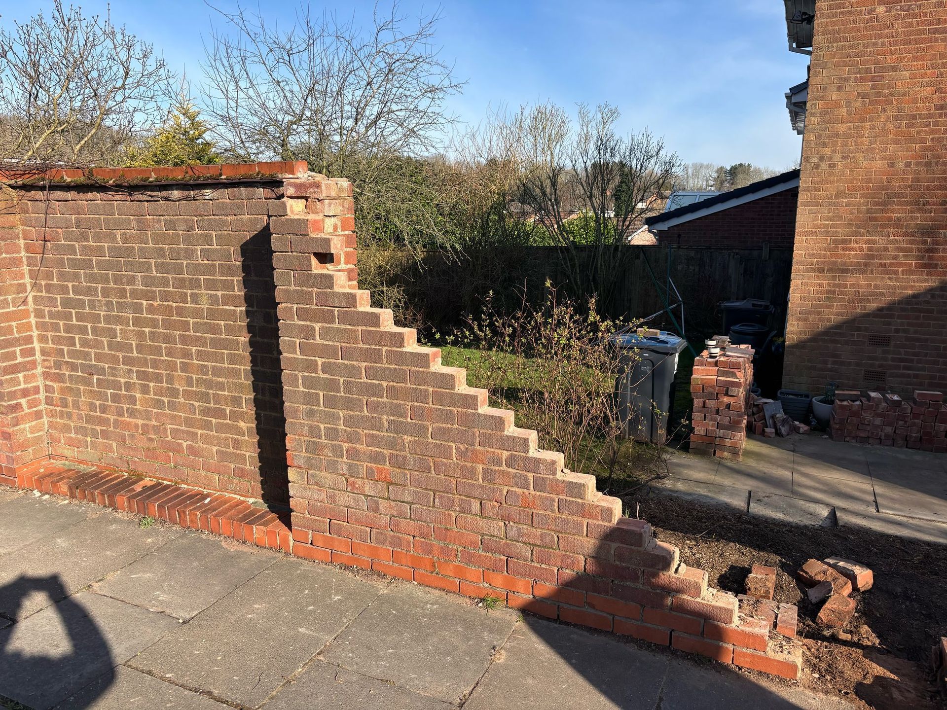 Brick wall with a stepped edge beside a driveway and house in a sunny yard