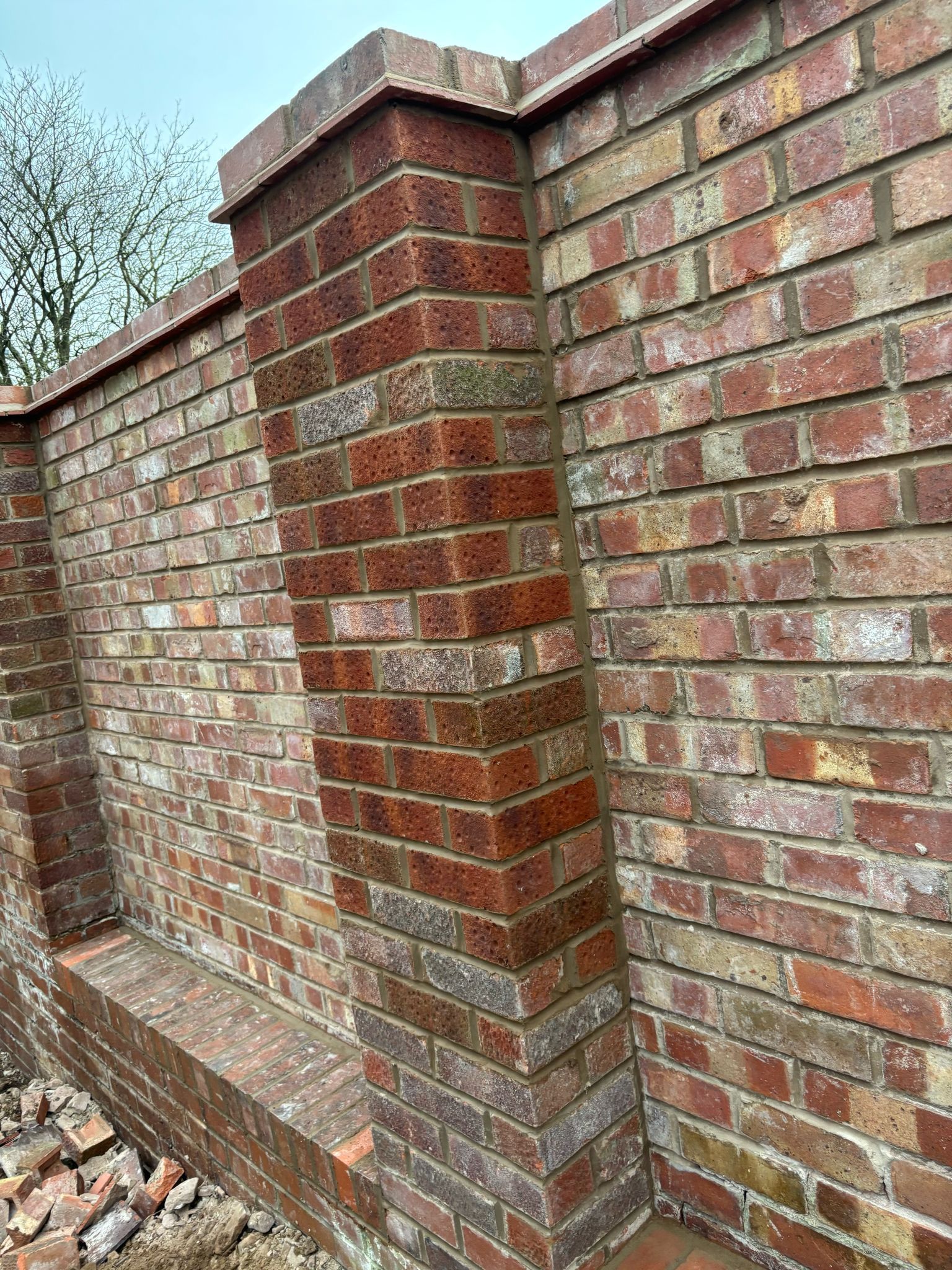 Red brick garden wall with a square pillar and curved sections, seen from a slight angle.