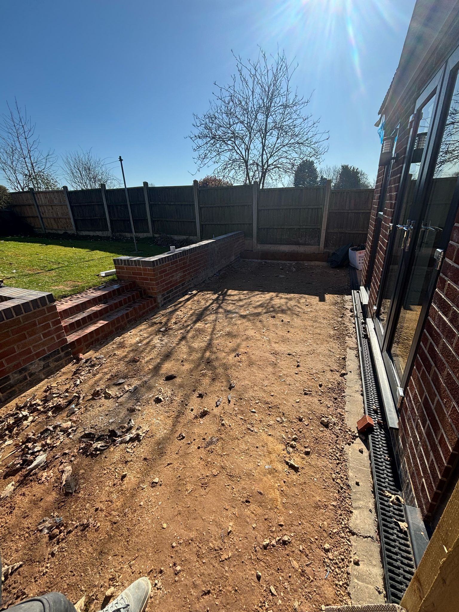Sunny backyard with a dirt patio area, brick edging, and wooden fence panels.