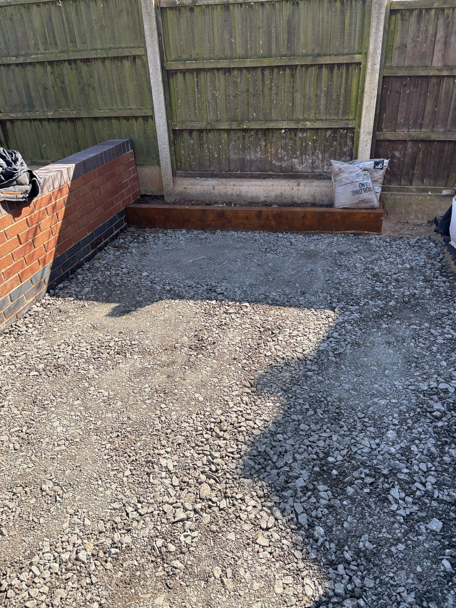 Backyard with gravel patio area, raised brick border, and wooden fence in the background