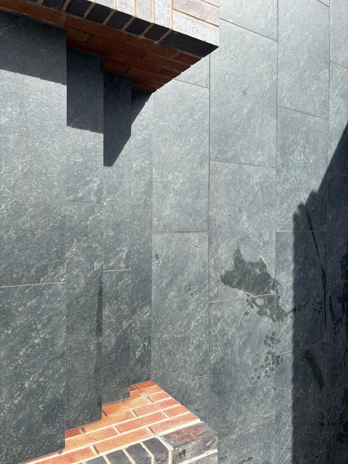 Dark slate wall with a small brick opening and roof overhang casting shadows