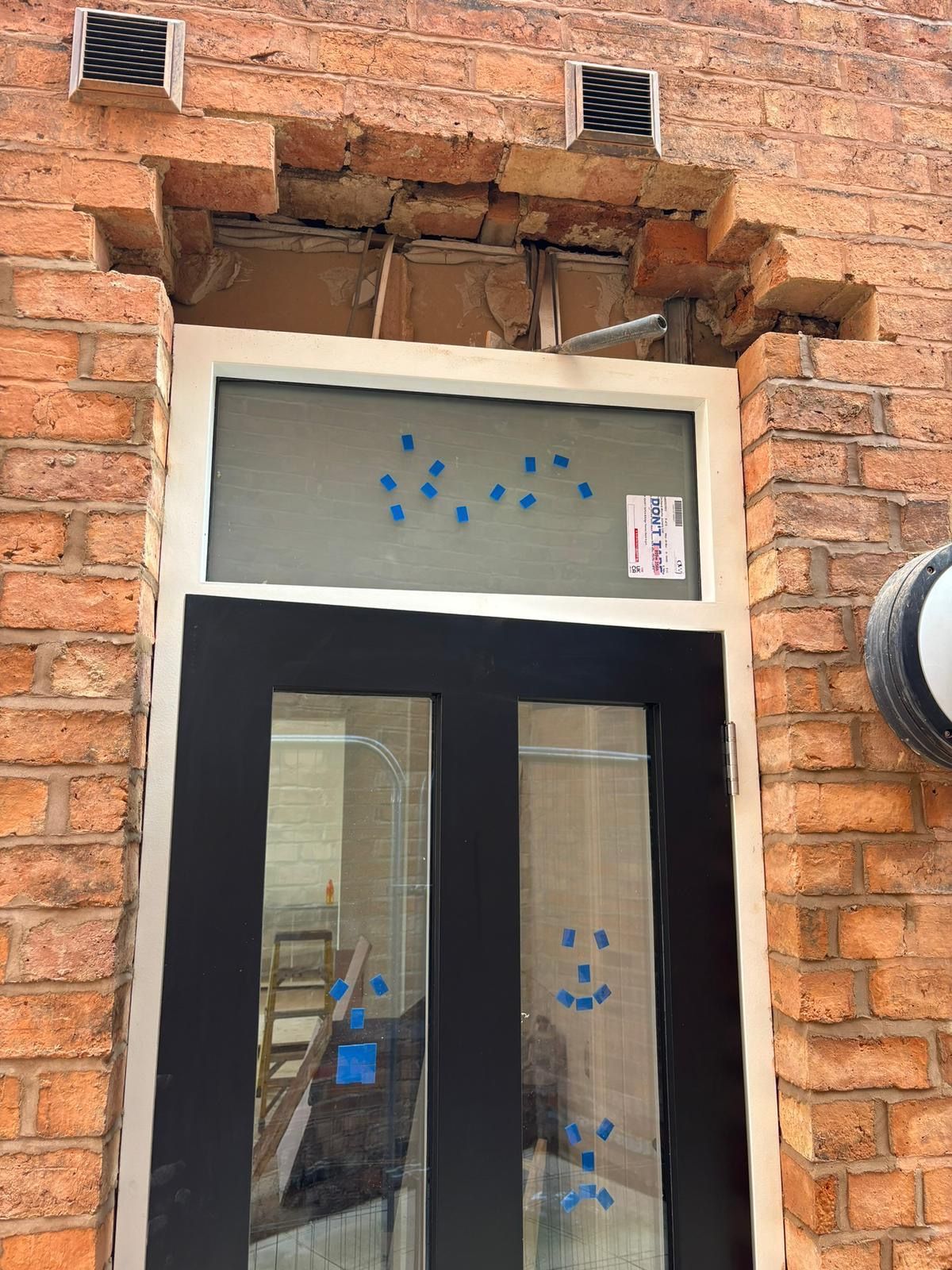 Damaged brick storefront entrance with black-framed glass door and window, and a damaged arch above it
