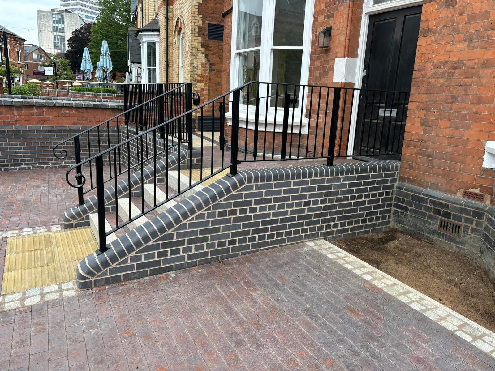 Brick ramp with black railings leading to a building entrance beside a brick courtyard