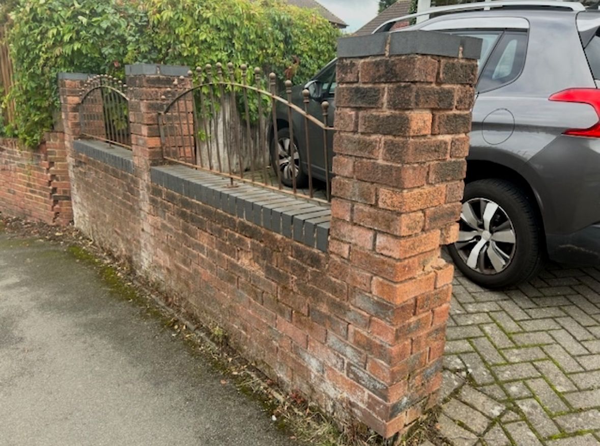 Brick garden wall with iron fence beside a driveway and parked gray SUV