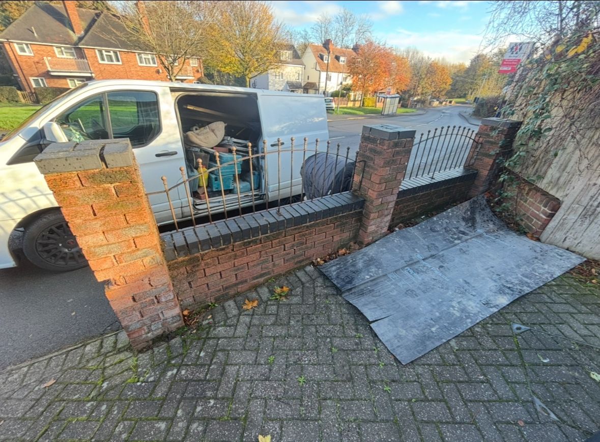 White van parked by a brick wall and black gate beside a sloped sidewalk and driveway mat