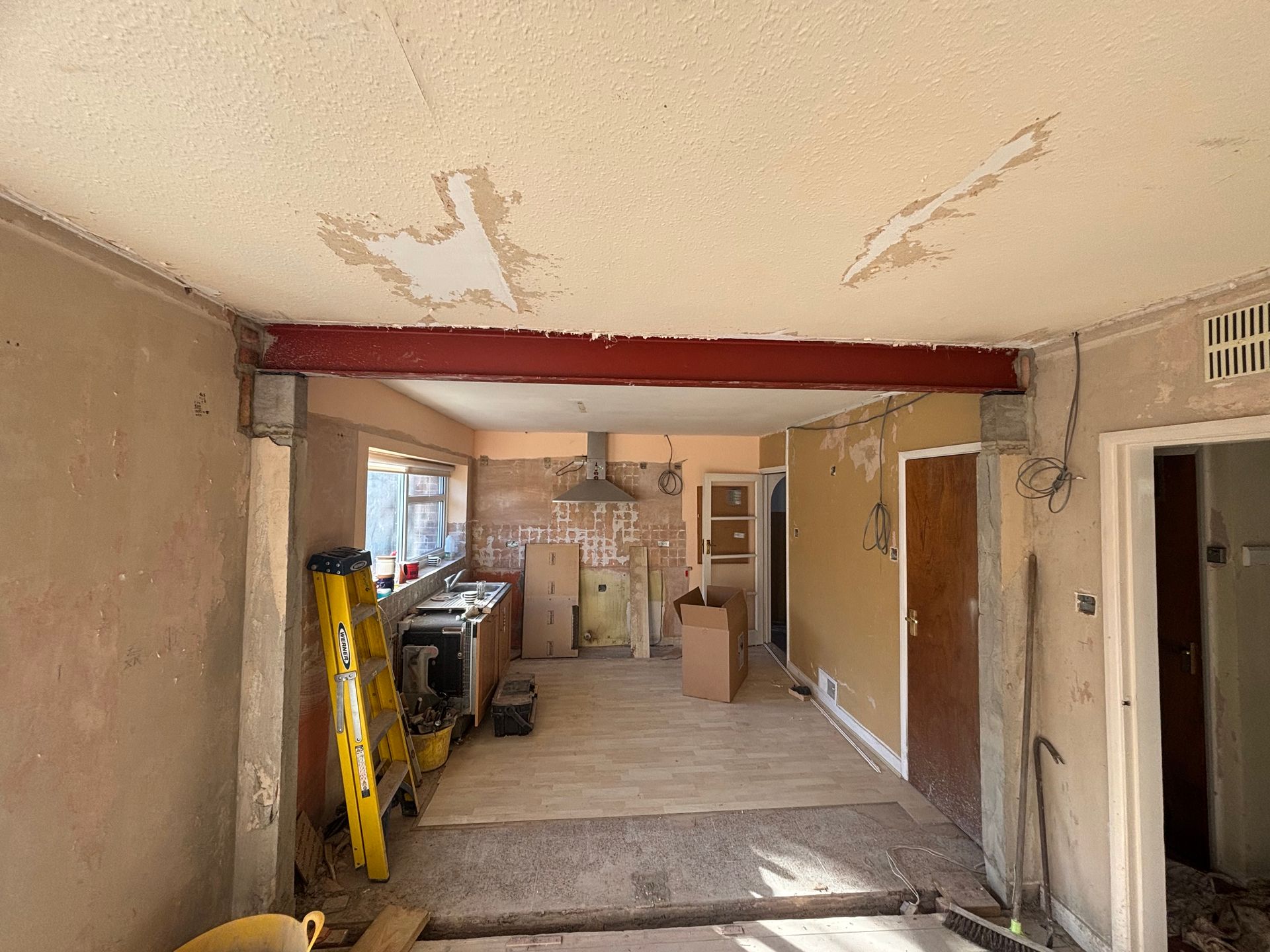 Renovation site with exposed ceiling, ladder, tools, and unfinished walls in a narrow room