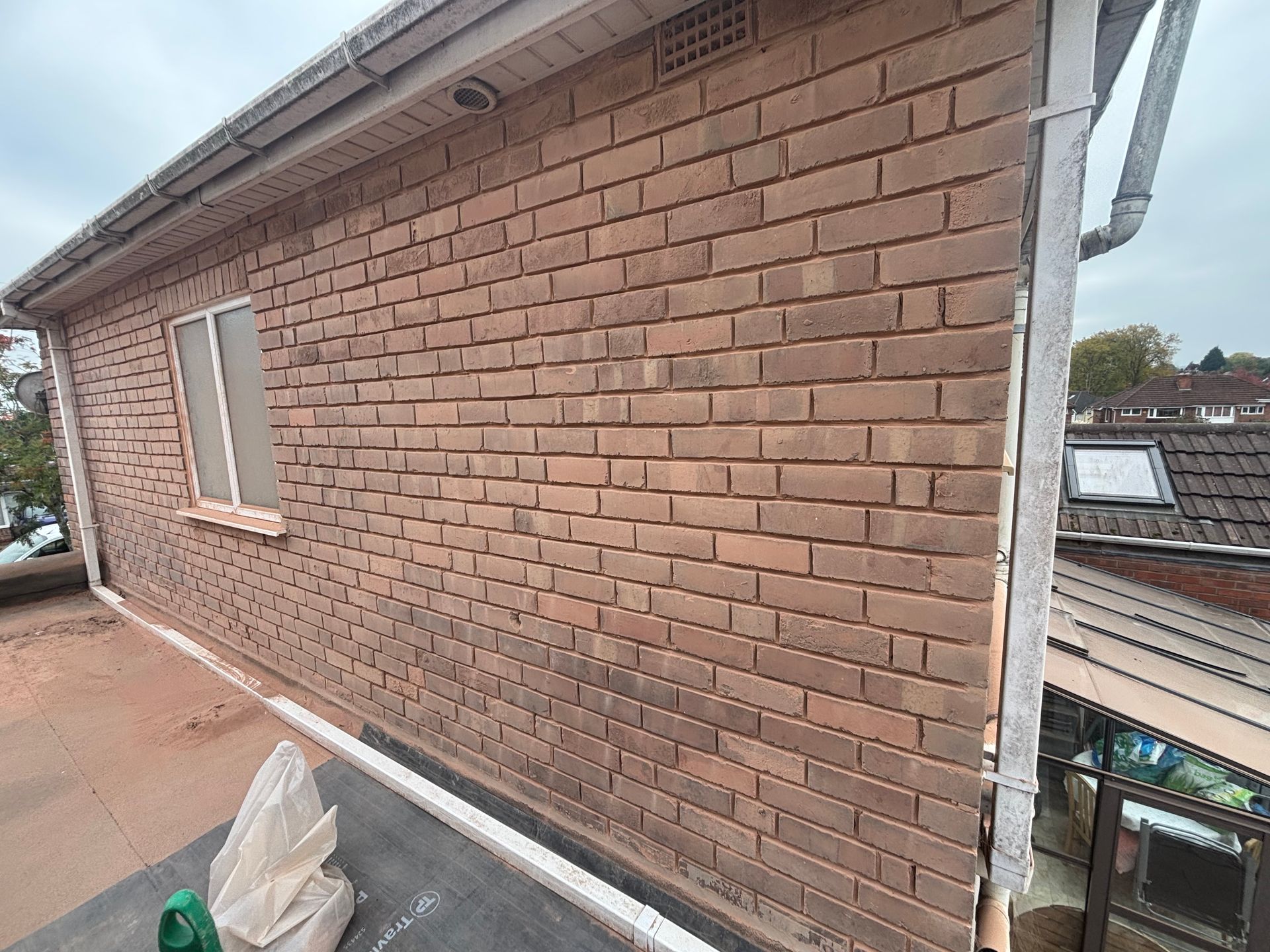 Side view of a brick house exterior with a window and roof gutter, on a construction site.