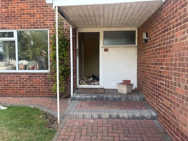 Brick house entrance with front steps, open doorway, and a small porch under a covered awning