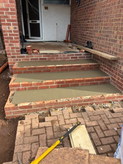 Brick front steps with broken, uneven concrete landing leading to a white door.