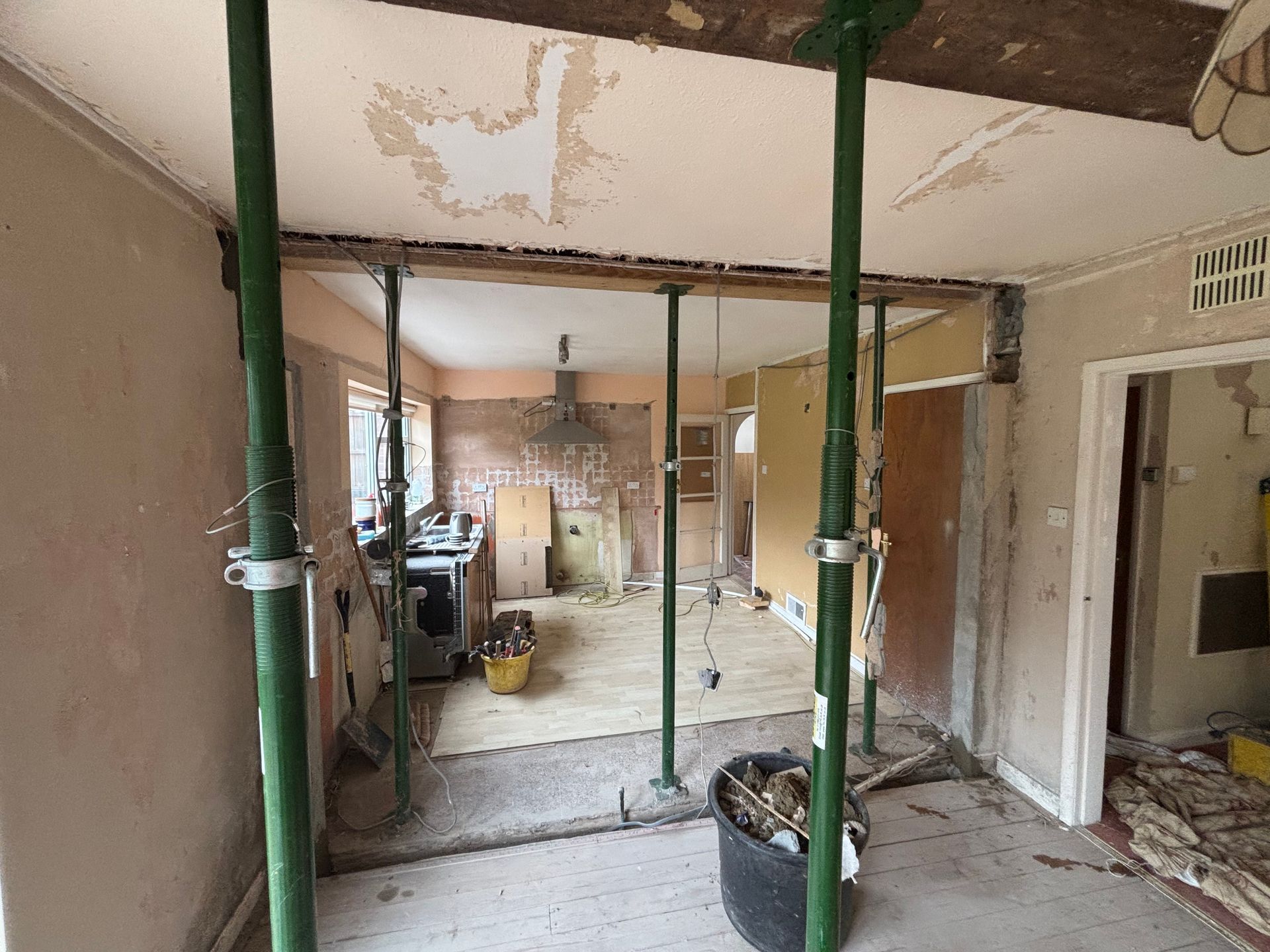 Interior of a stripped room under renovation with exposed studs, peeling walls, and construction materials.