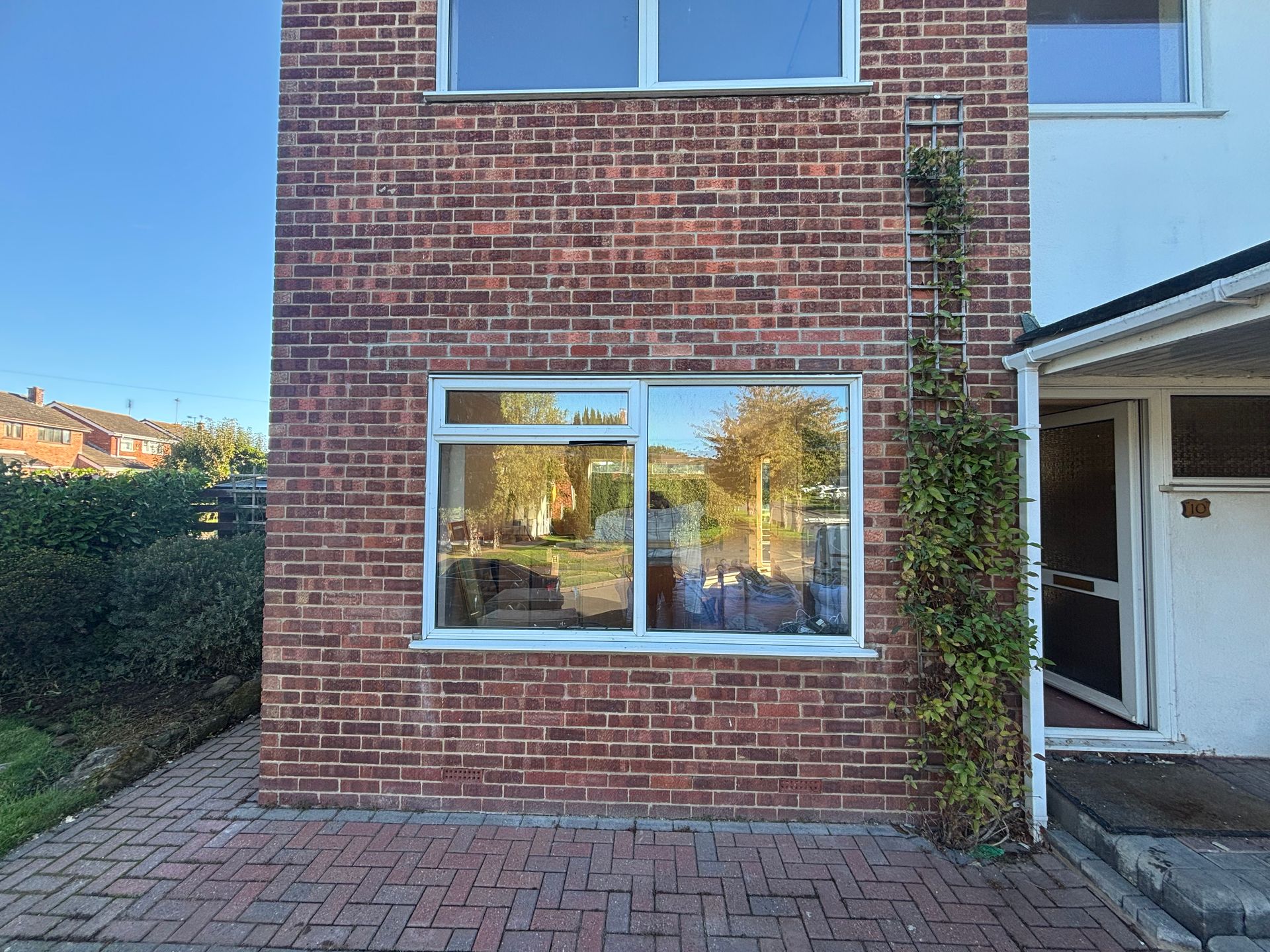Brick townhouse exterior with a white-framed window, paved patio, and vine-covered wall.