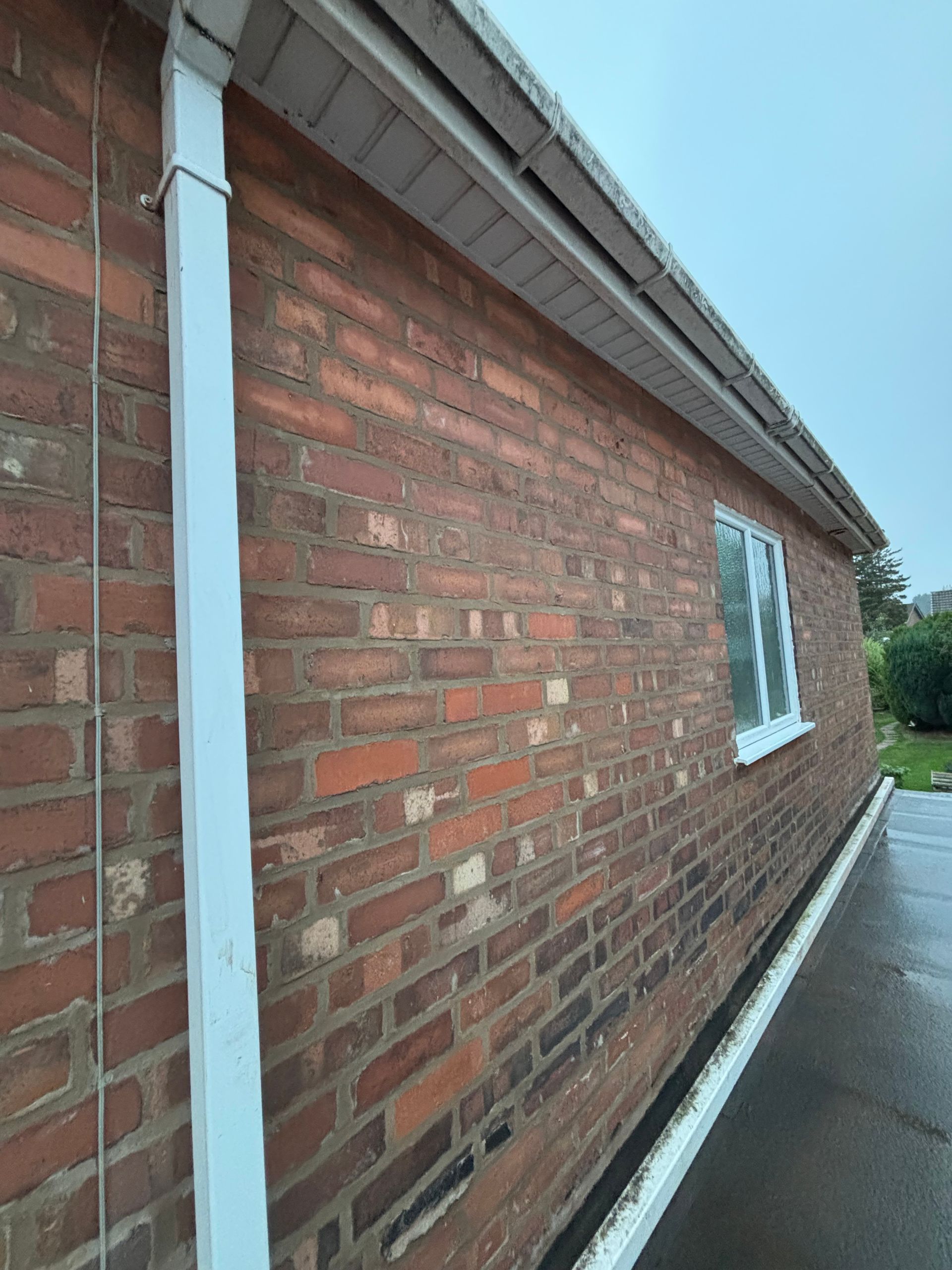 Brick building side wall with white gutter and a narrow sidewalk beside it