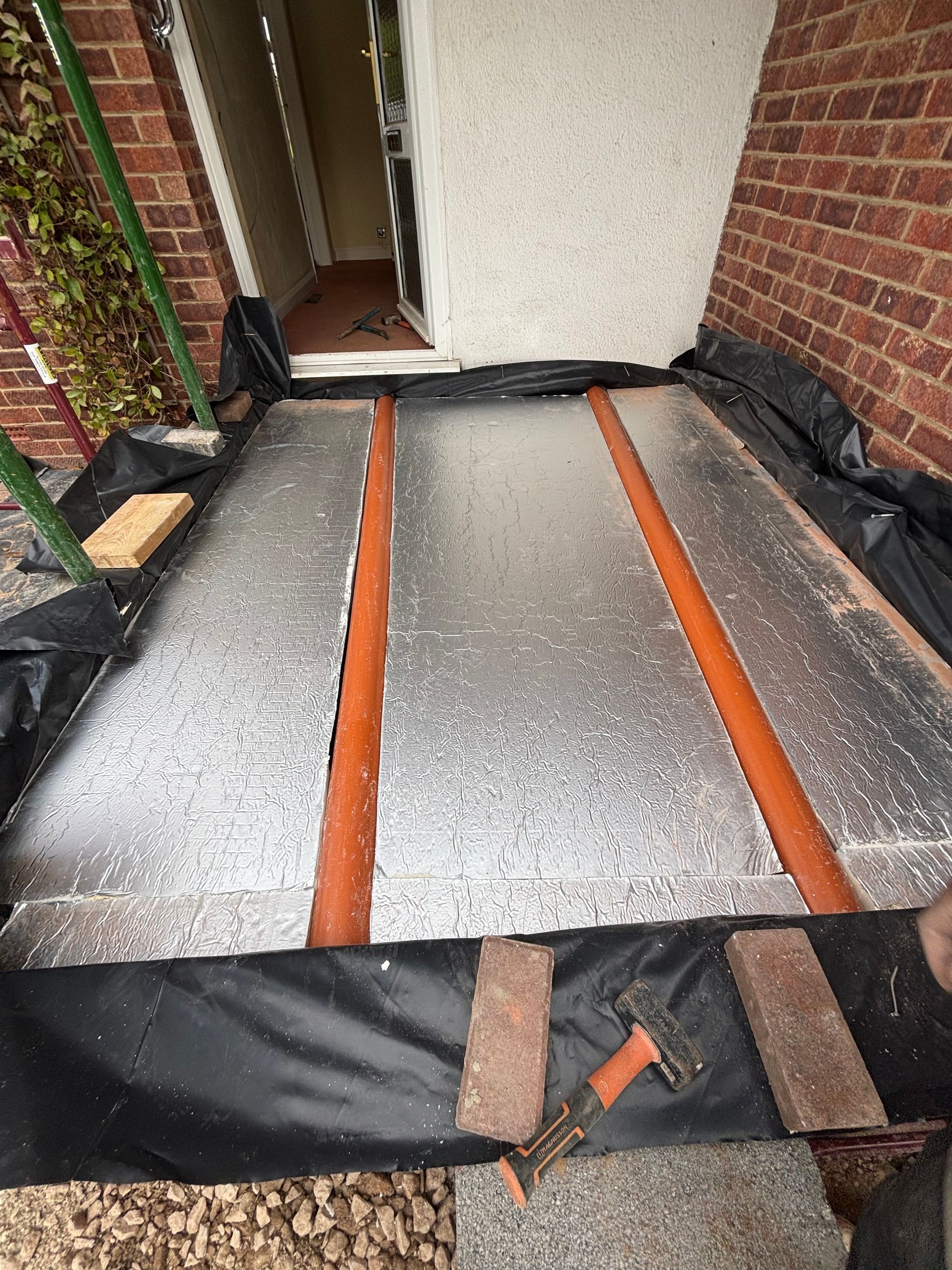 Roofing repair with black underlayment and orange battens beside brick walls and a white door