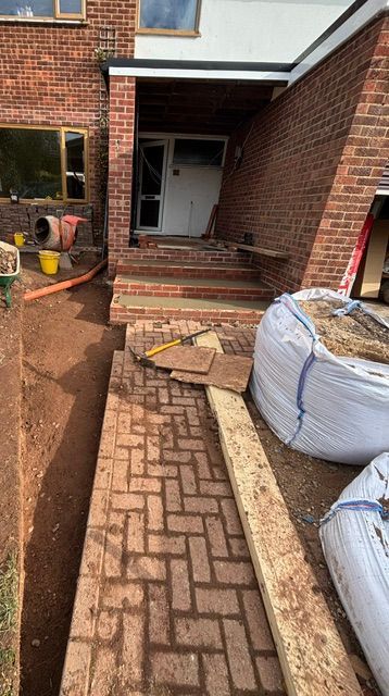 Brick house entrance with steps, open front door, and a narrow paved path under construction
