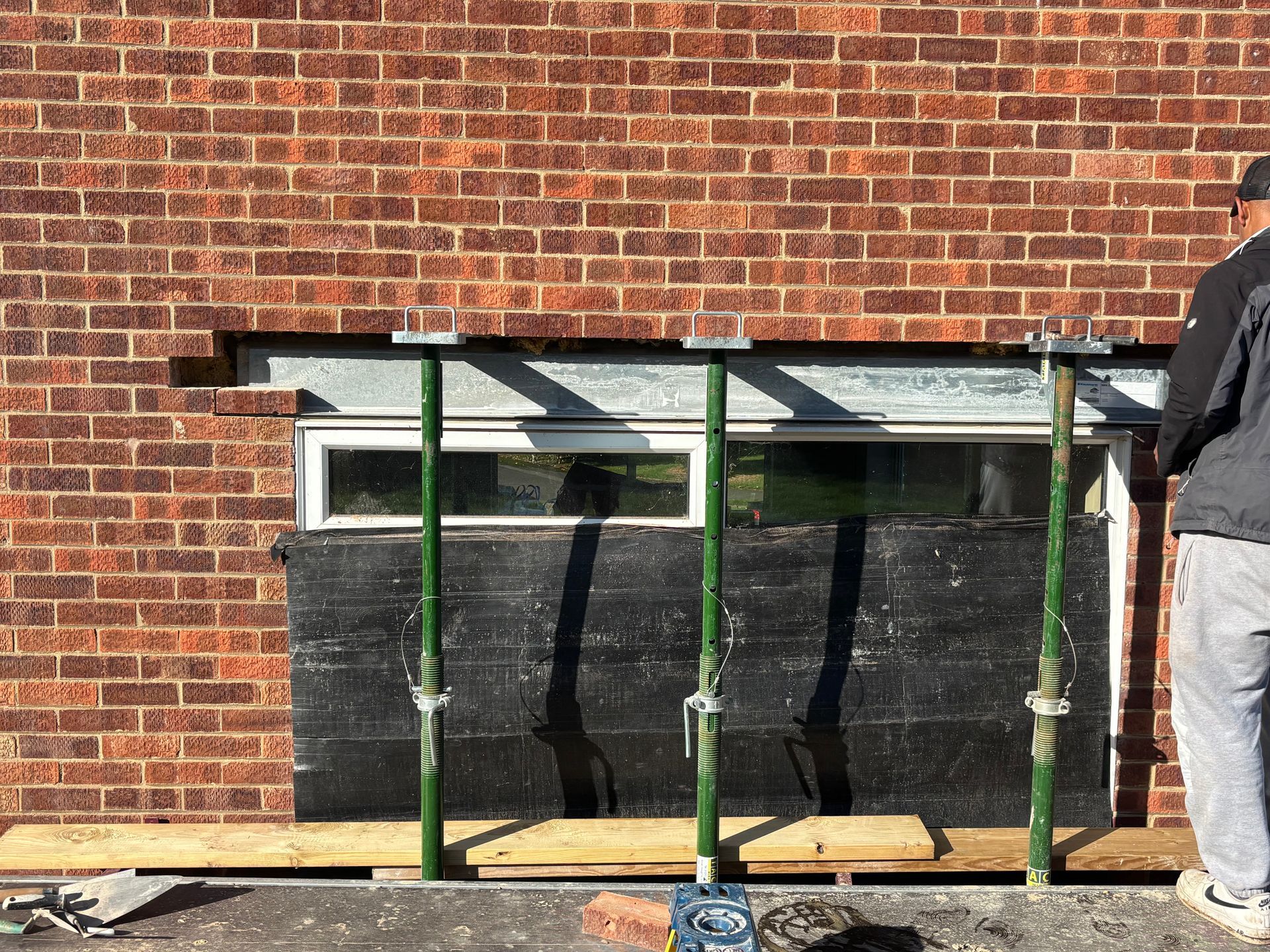 Green scaffold in front of a brick wall and window, with a person partially visible at right