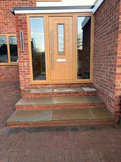 Front entrance with a wooden door, glass sidelights, and brick steps leading up to it.