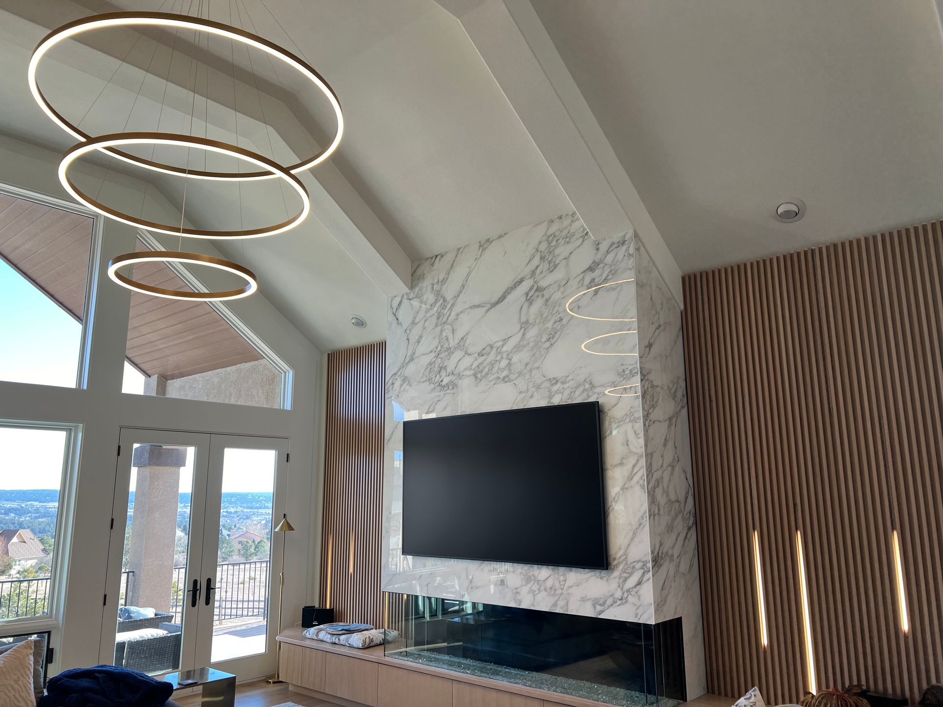 Modern living room with marble fireplace, large TV, and ring-shaped lights. Wooden paneling on walls.
