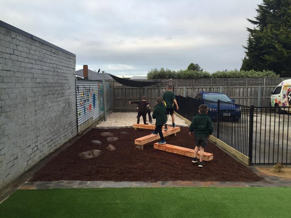 Children planting in a schoolyard garden bed beside a fence and wall