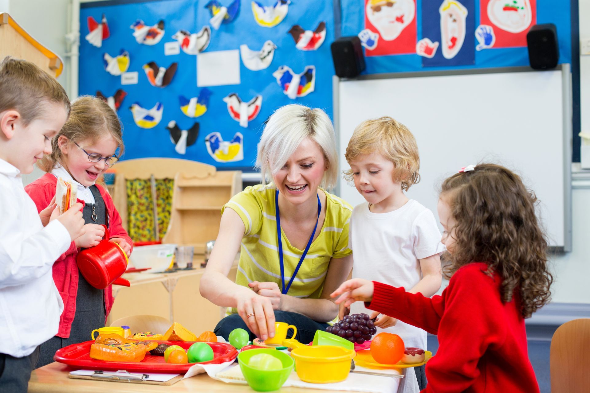 Children and teacher sharing fruit at a colorful classroom snack table