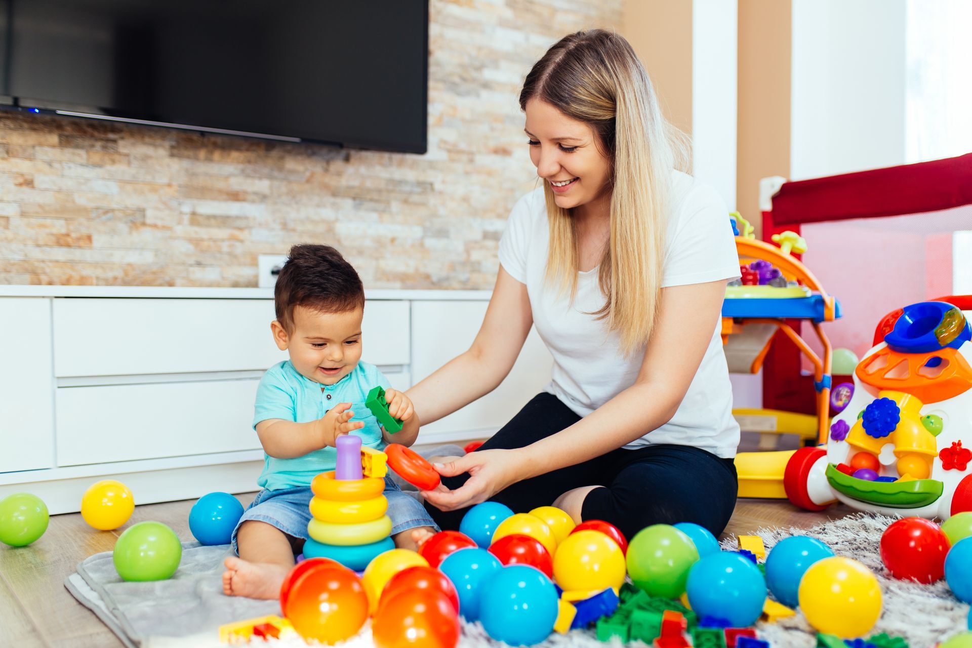 Woman and toddler playing with colorful toys on the floor in a bright living room